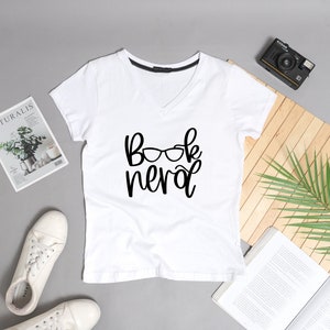May include: White v-neck t-shirt with the text "Book Nerd" and a pair of glasses graphic printed on the front.