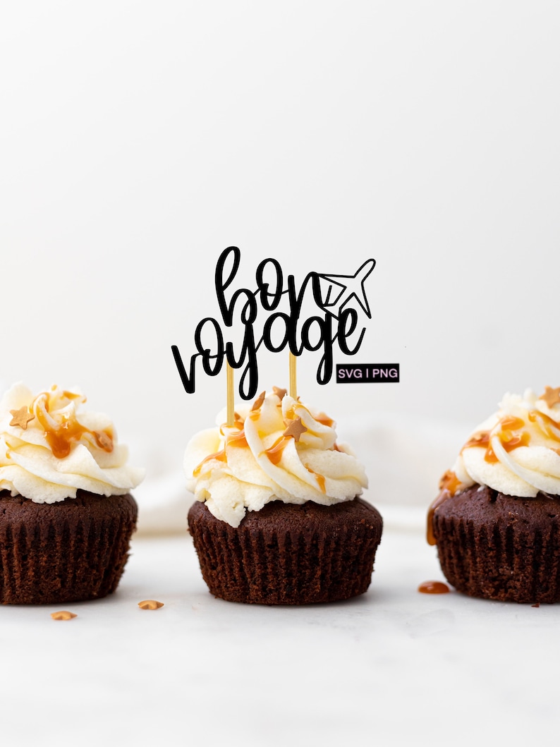 May include: Three chocolate cupcakes with white frosting and caramel drizzle topped with gold star sprinkles. A black and white cupcake topper with the text "bon voyage" and a small airplane graphic is on the middle cupcake.
