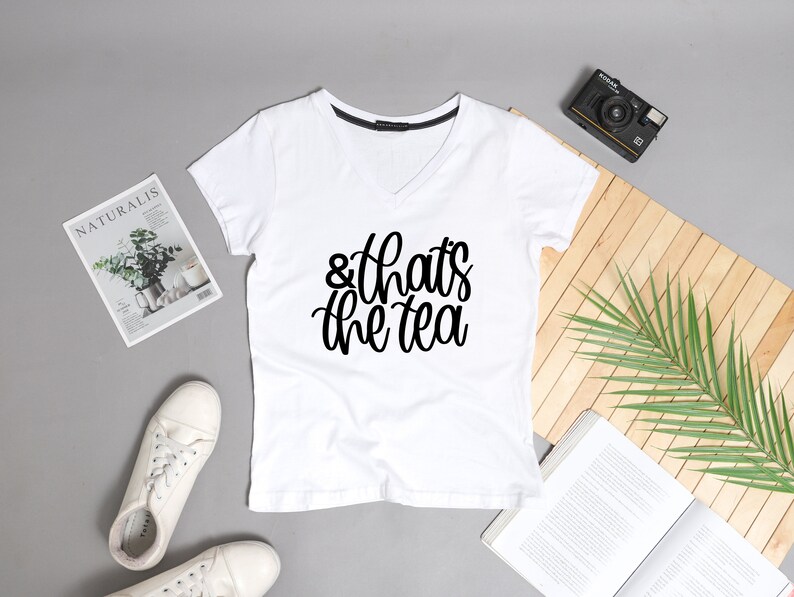 May include: White v-neck t-shirt with the text "& that's the tea" printed in black.