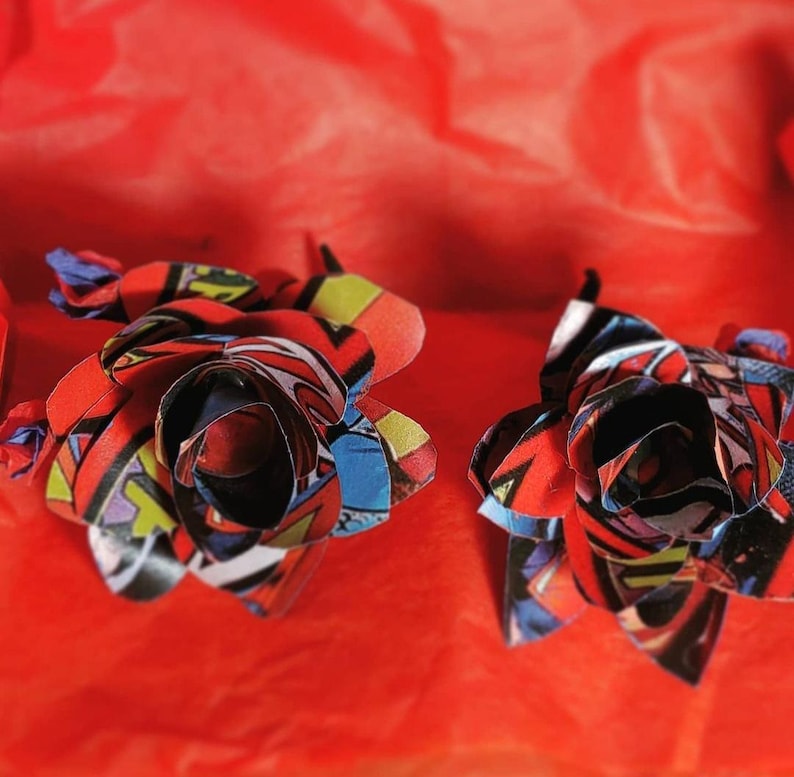 May include: Two red, blue, and yellow paper roses made from comic book pages. The roses are on a red background.