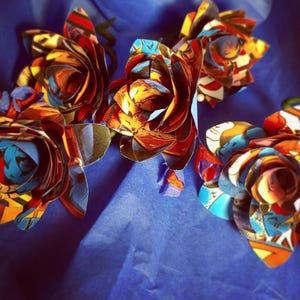 May include: Four handmade paper roses made from colorful comic book pages. The roses are arranged on a blue background.