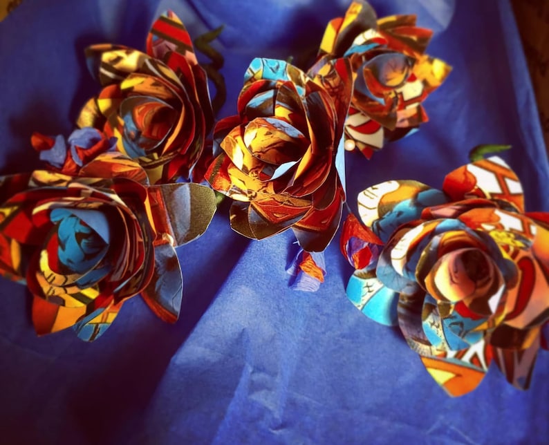 May include: Four handmade paper roses made from colorful comic book pages. The roses are arranged on a blue background.