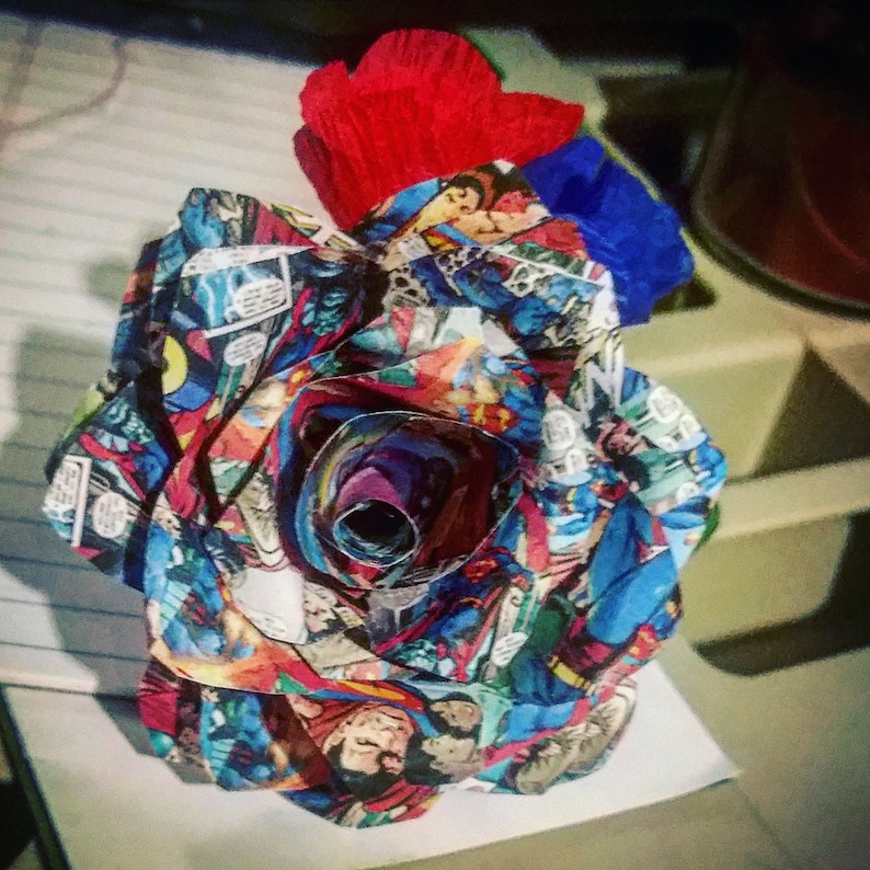 May include: A red, white, and blue paper rose made from comic book pages. The rose is curled into a spiral shape and has a red and blue paper bow on top.