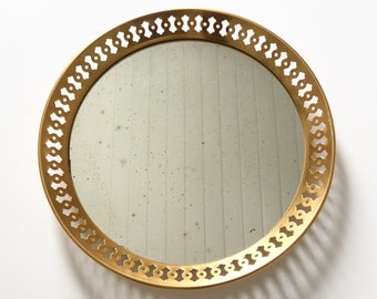 Peut inclure: Un miroir rond doré avec un cadre décoratif et orné. Le cadre présente un motif répétitif de petites formes arrondies.