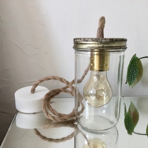 Könnte beinhalten: Ein klares Glasgefäß mit einem Metalldeckel und einer Glühbirne, die an dem Deckel hängt. Das Gefäß ist an einem braunen Seil befestigt.