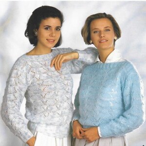 May include: Two women in light blue knitted sweaters with boat necks and long sleeves. The sweaters feature a textured, openwork pattern. One woman leans on the other, both smiling. The sweaters are a soft, pastel blue.