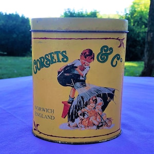 Keller Charles of Philadelphia Corsets & Co Yellow Tin-Norwich England-Boy Watering Girls Sitting Under Umbrella w Puppy-Collectible Tin