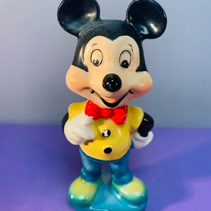 Pu&ograve; includere: Una statuetta in ceramica vintage di Topolino con una camicia gialla, pantaloni blu e un papillon rosso. Ha un grande sorriso ed &egrave; in piedi con le mani sui fianchi.