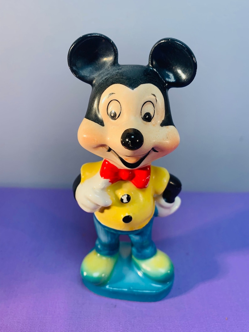Pu&ograve; includere: Una statuetta in ceramica vintage di Topolino con una camicia gialla, pantaloni blu e un papillon rosso. Ha un grande sorriso ed &egrave; in piedi con le mani sui fianchi.