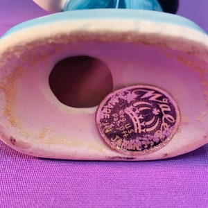 Pu&ograve; includere: Primo piano del fondo di una statuetta in ceramica. La statuetta ha un foro sul fondo e un adesivo dorato con il testo "Made in Japan Reg. U.S. Pat. Off.", una corona e la parola "Waller" in un cerchio.
