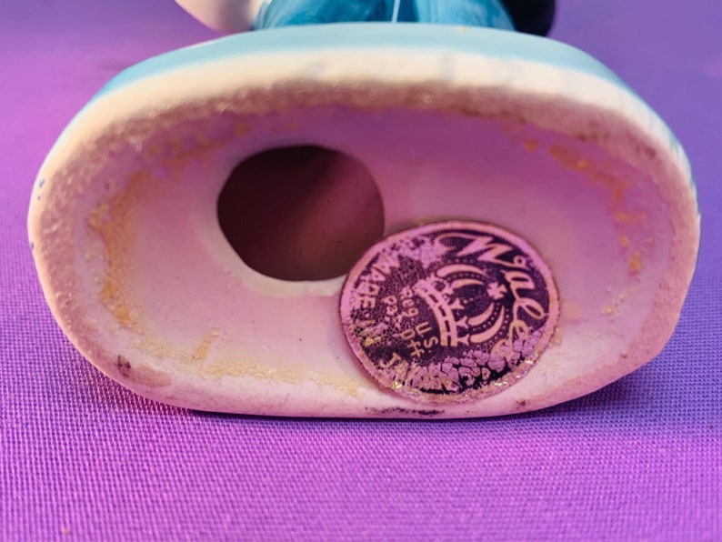 Pu&ograve; includere: Primo piano del fondo di una statuetta in ceramica. La statuetta ha un foro sul fondo e un adesivo dorato con il testo "Made in Japan Reg. U.S. Pat. Off.", una corona e la parola "Waller" in un cerchio.