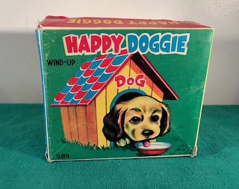 May include: Vintage wind-up toy dog in a red and blue doghouse. The box is green with the words "Happy Doggie" and "Wind-Up" printed on it. The toy is labelled "Dog" and "Made in Japan".
