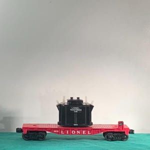 May include: A red Lionel Transformer Car with black wheels and a black transformer. The transformer has white accents and the words "Lionel Transformer Car" printed on it. The car is a vintage toy.