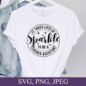 May include: White t-shirt with a black circle design that says "It takes lots of sparkle to be a teacher assistant".