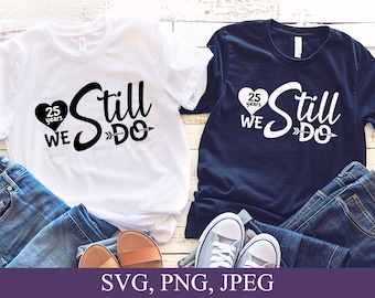 May include: Two white and navy blue t-shirts with the text "Still We Do" and a heart with the text "25 years" on them. The shirts are laid out on a wooden surface with jeans and sandals.