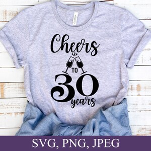 May include: A light gray t-shirt with the words "Cheers to 30 years" in black script and a graphic of two champagne flutes clinking. The number 30 is large and bold. The bottom of the image shows the text "SVG, PNG, JPEG".