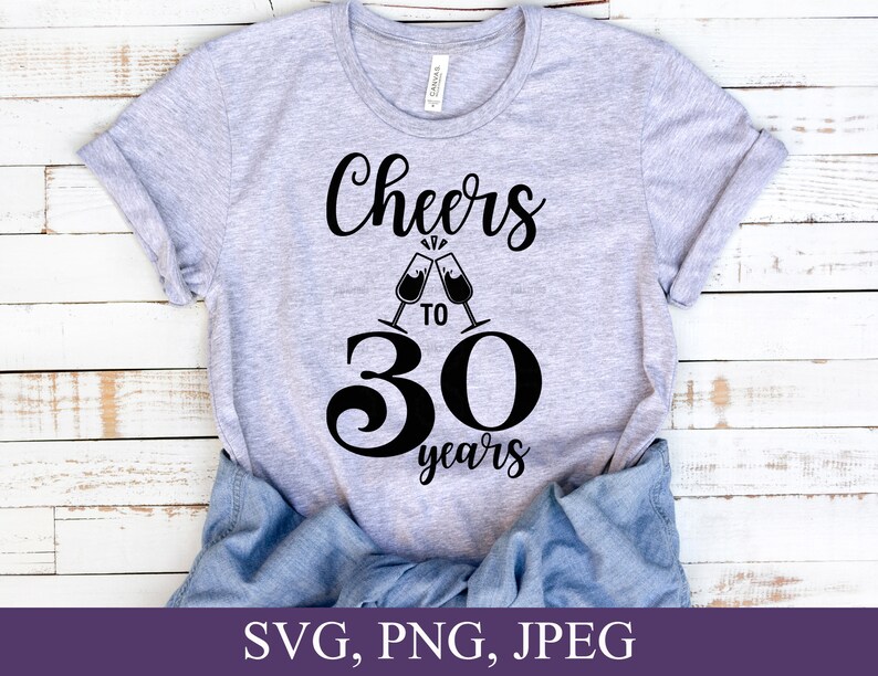 May include: A light gray t-shirt with the words "Cheers to 30 years" in black script and a graphic of two champagne flutes clinking. The number 30 is large and bold. The bottom of the image shows the text "SVG, PNG, JPEG".