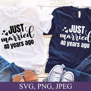 May include: Two white t-shirts with black text that reads "JUST married 40 years ago" and two black t-shirts with white text that reads "JUST married 40 years ago". The shirts are laid out on a wooden surface with blue jeans and sandals.