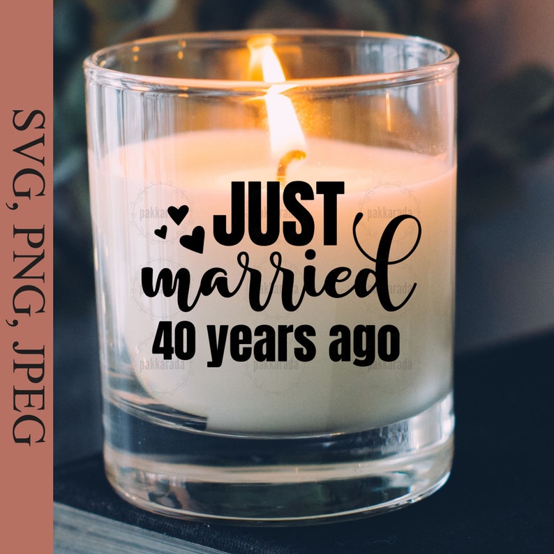 May include: A clear glass candle jar with a white candle inside. The candle has a black inscription that reads "JUST married 40 years ago" with two small hearts.