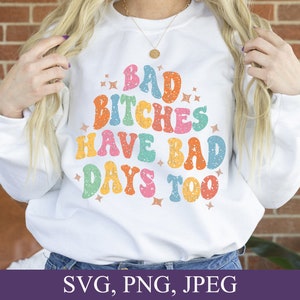 May include: White sweatshirt with a colorful retro-style graphic that says "Bad Bitches Have Bad Days Too".