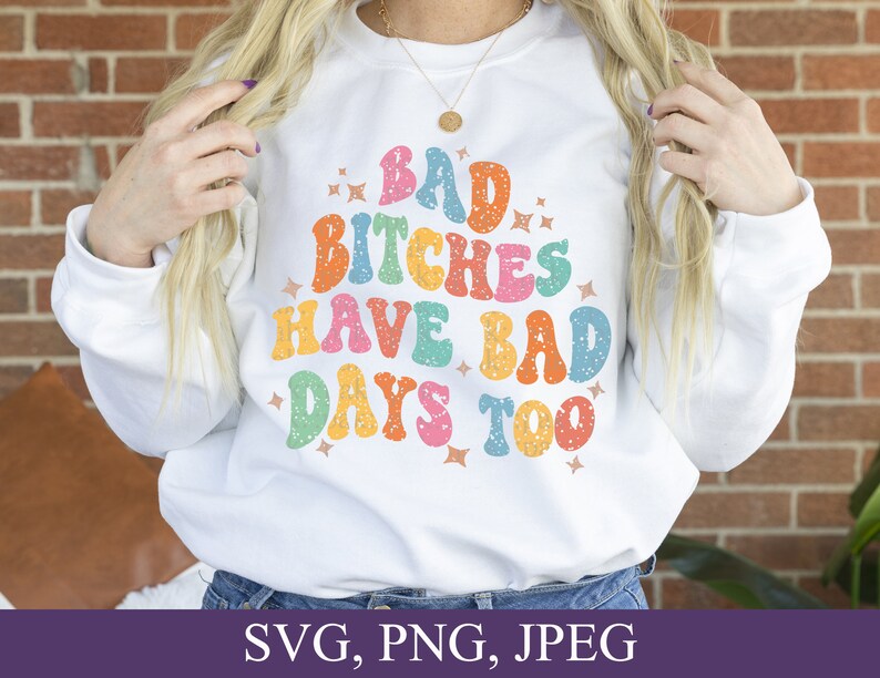 May include: White sweatshirt with a colorful retro-style graphic that says "Bad Bitches Have Bad Days Too".