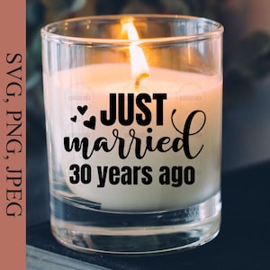 May include: A clear glass candle jar with a white candle inside. The candle has a black inscription that reads "JUST married 30 years ago" with two small hearts above the word "married".