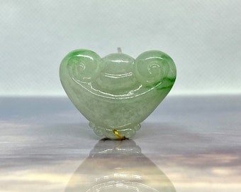 May include: A green jade pendant carved in the shape of a heart with a swirl design. The pendant is attached to a gold wire.