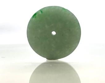 May include: A round, light green jade pendant with a hole in the center. The pendant has a smooth, polished surface and a subtle green swirl pattern.