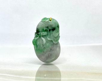 May include: A green jade pendant carved in the shape of a gourd with a gold loop at the top. The gourd is decorated with intricate carvings and has a light green and white color.