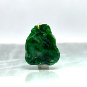 Pode incluir: Um pingente de jade verde esculpido com um design em espiral. O pingente está preso a um cordão dourado.