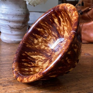 May include: A brown and yellow ceramic bowl with a mottled glaze. The bowl is sitting on a wooden table.