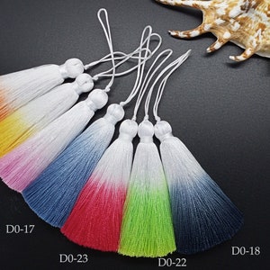May include: Seven ombre tassel charms with white tips. The tassels are in the following colors: orange, yellow, pink, blue, red, green, and dark blue. The tassels are labeled with the following codes: D0-21, D0-20, D0-19, D0-17, D0-23, D0-22, and D0-18.