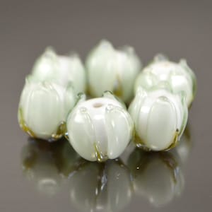May include: A set of six white glass beads with green accents, shaped like flowers. The beads are arranged in a circle.