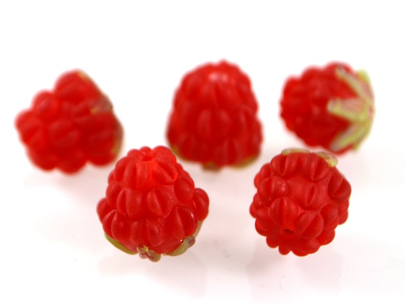 May include: Five red glass beads shaped like raspberries. The beads are smooth and shiny.