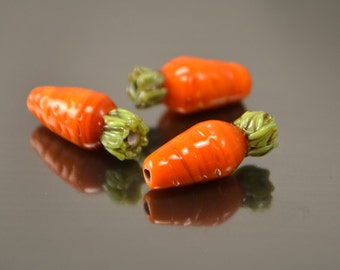 May include: Three glass carrot beads with green tops. The beads are orange and have a ribbed texture.