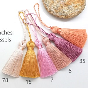 Può includere: Sei frange di 5 cm di lunghezza in vari colori, tra cui rosa, pesca, oro e rosa chiaro. Le frange sono disposte in una fila da sinistra a destra, con i numeri 78, 15, 7, 5, 35 e 77 scritti sotto.