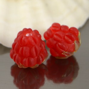 May include: Two red glass beads shaped like raspberries. The beads have a textured surface and are slightly translucent.