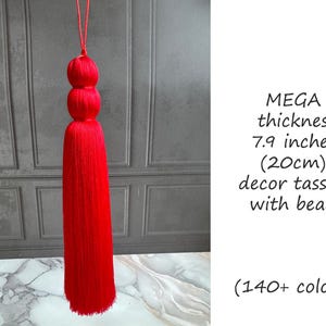 May include: A vibrant red decor tassel with a thickness of 7.9 inches (20cm). The tassel features three spherical beads at the top and is suspended by a matching red cord. The image includes text that reads "MEGA thickness decor tassels with beads."