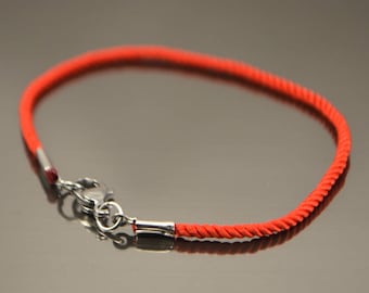 May include: A red string bracelet with a silver clasp. The bracelet is made of a thin, braided cord.