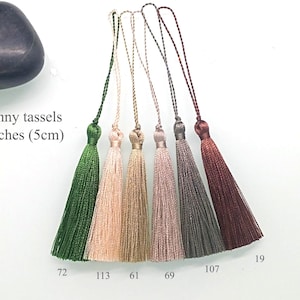 May include: Five skinny tassels in different colors: green, beige, pink, gray, and burgundy. Each tassel is 2 inches (5 cm) long. The tassels are arranged in a row from left to right. The numbers 72, 113, 61, 69, 107, and 19 are written below the tassels.
