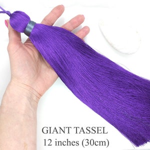Pode incluir: Um grande e vibrante pendão roxo, com aproximadamente 30 cm de comprimento, com uma argola no topo. O pendão é exibido sobre um fundo branco. O texto "GIANT TASSEL" e "12 inches (30cm)" são visíveis.
