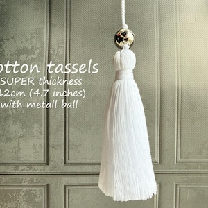 May include: White cotton tassel with a metal ball detail, suspended against a textured backdrop. The image text states "Cotton tassels SUPER thickness 12cm (4.7 inches) with metall ball."
