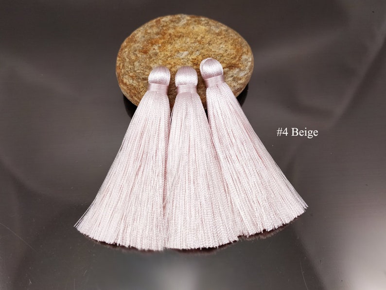 May include: Three light pink silk tassels with a beige background. #4 Beige