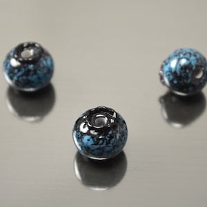 Puede incluir: Tres cuentas redondas de vidrio azul y negro con manchas y un agujero en el centro.