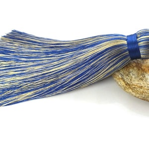 May include: A blue and gold tassel with a blue satin knot. The tassel is made of thin strands of yarn and is about 10 inches long.