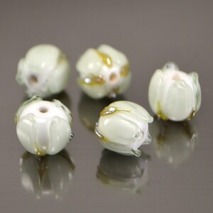 May include: Five white glass beads with a green and gold swirl design. The beads are round and have a slightly irregular shape.