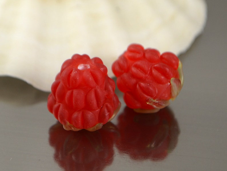 May include: Two red glass beads shaped like raspberries. The beads are translucent and have a glossy finish.