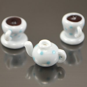 Puede incluir: Una tetera blanca y dos tazas de t&eacute; blancas con lunares azules. La tetera tiene un pico y una manija. Las tazas de t&eacute; tienen asas y est&aacute;n sentadas sobre platillos.