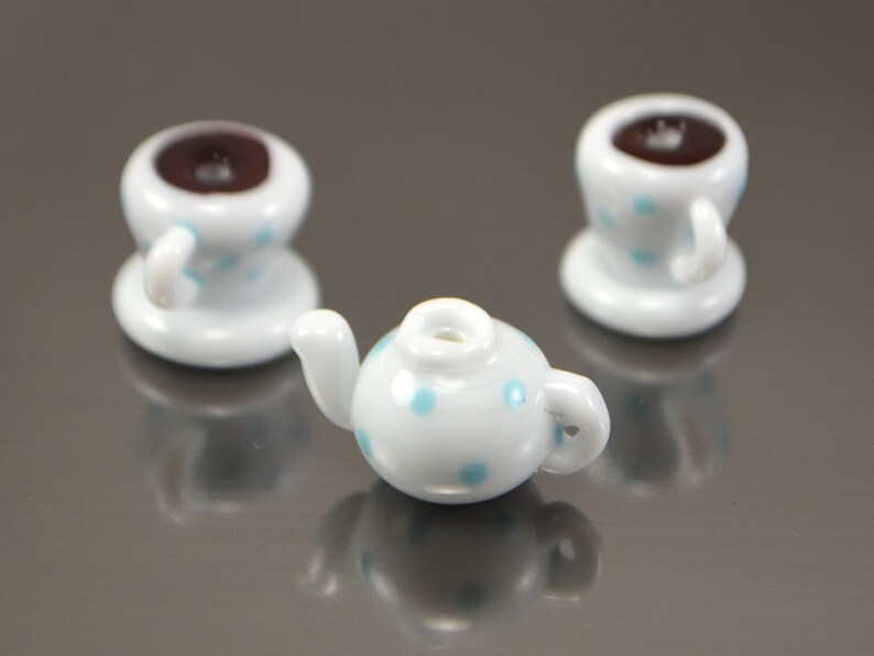 Puede incluir: Una tetera blanca y dos tazas de t&eacute; blancas con lunares azules. La tetera tiene un pico y una manija. Las tazas de t&eacute; tienen asas y est&aacute;n sentadas sobre platillos.