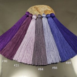 May include: Seven different shades of purple and blue tassels, arranged in a semi-circle on a light brown surface. The tassels are labeled with numbers: #9, #90, #21, #84, #86, #89, and #59.